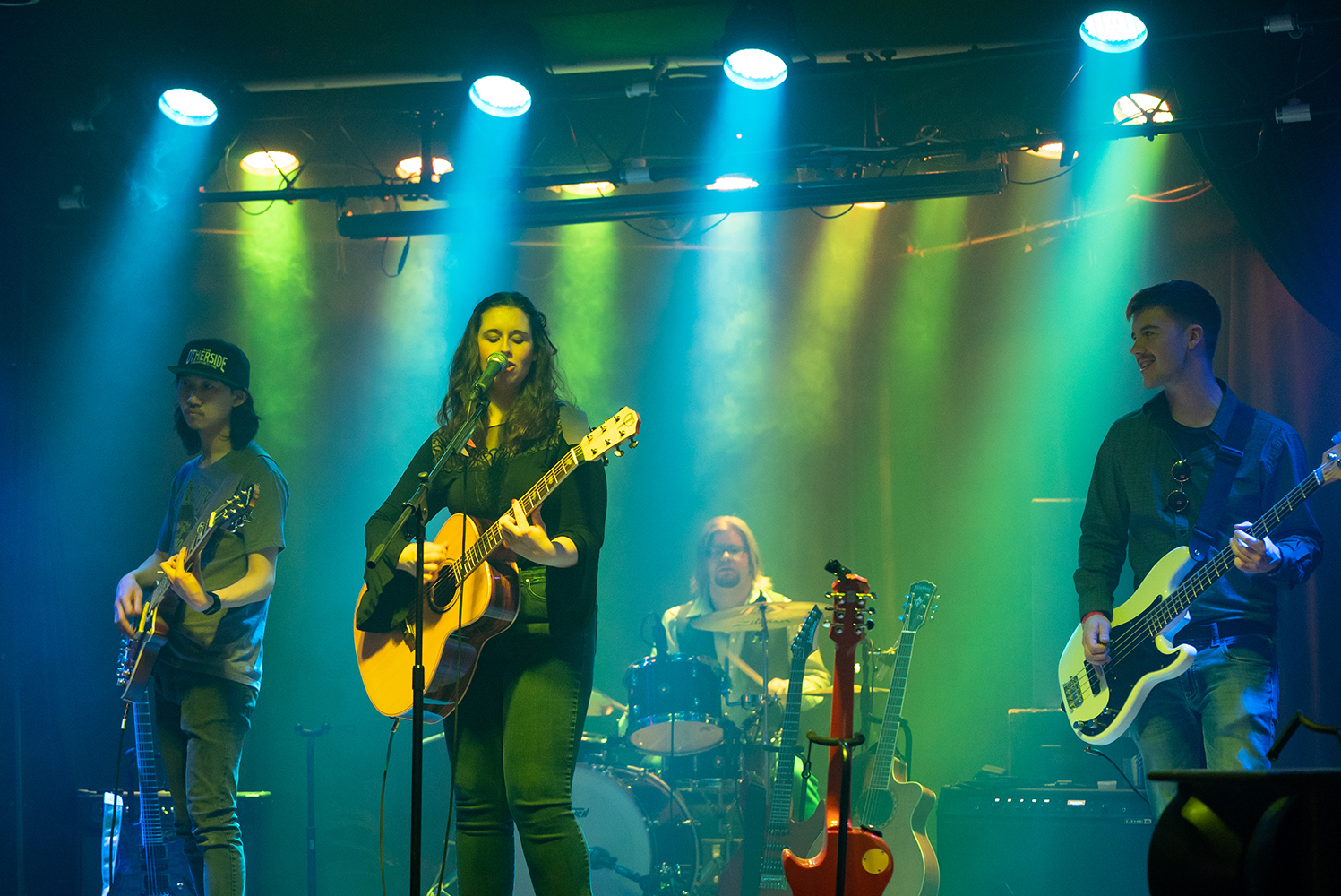 A group of young musicians playing on a colorfully lit stage.