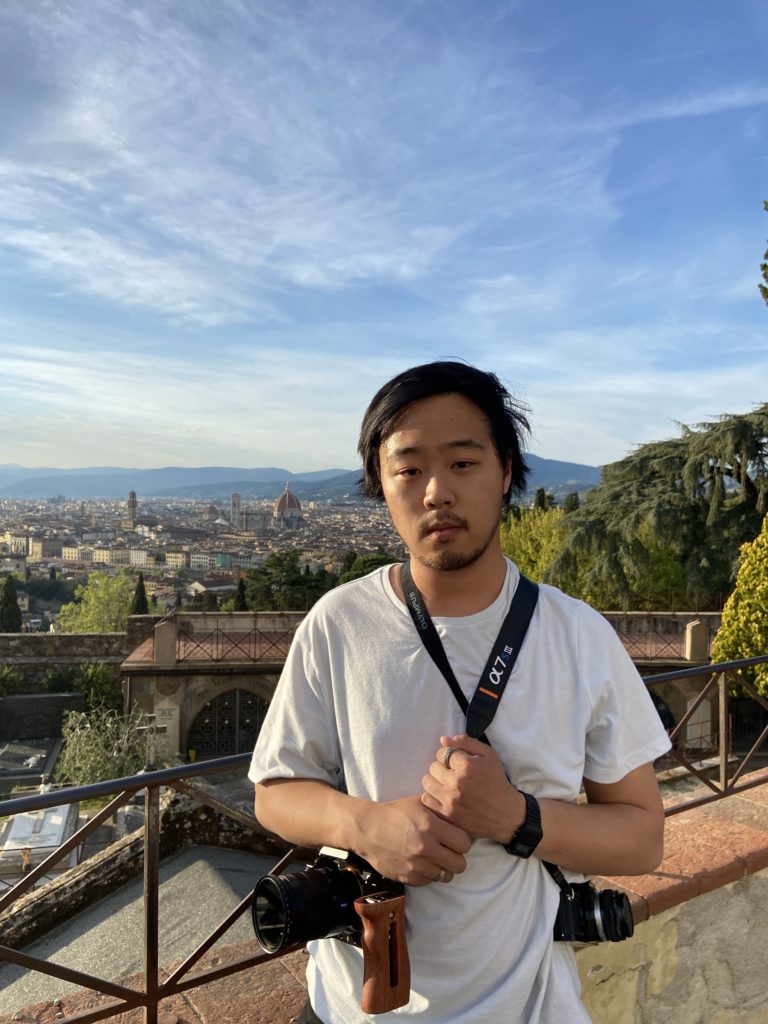 A young man in a white shirt poses against a cityscape.